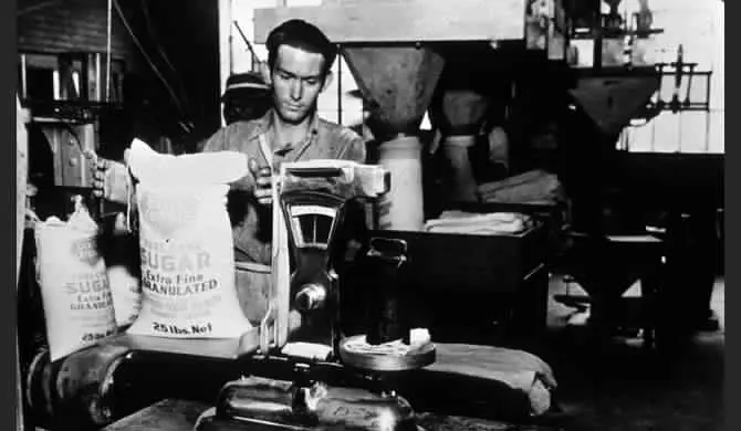 A vintage image of a man loading bags of sugar in a mill